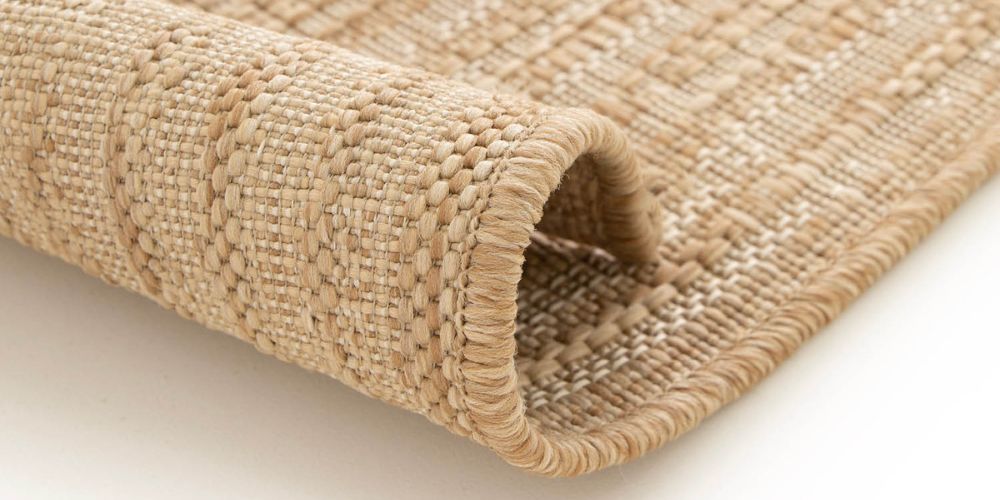 Nahaufnahme eines zusammengerollten beigen Outdoor-Teppichs mit sichtbarer Jute-Optik-Webstruktur
